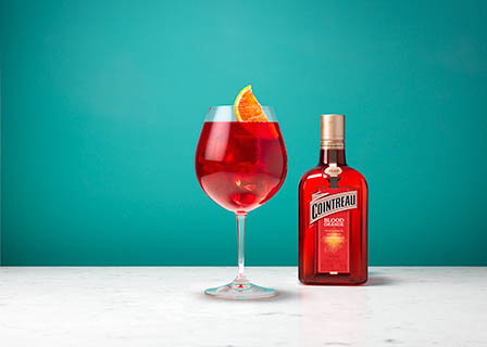Coloured background Explorer of Cointreau Blood Orange bottle and cocktail serve